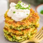 Close up square image of stacked Fritters on plate topped with sour cream and chives.