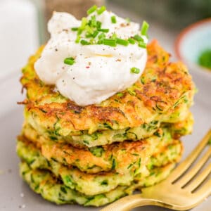 Close up square image of stacked Fritters on plate topped with sour cream and chives.