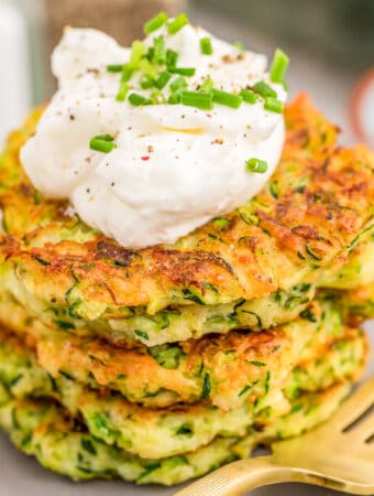 Close up square image of stacked Fritters on plate topped with sour cream and chives.