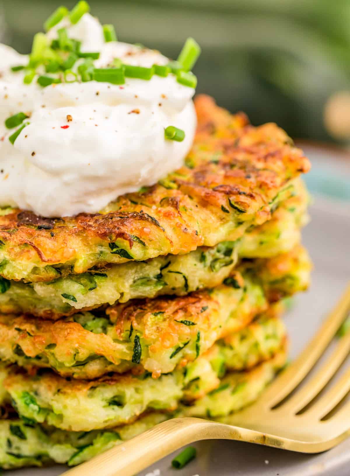 Close up side image of stacked fritters on plate topped with sour cream and chives.