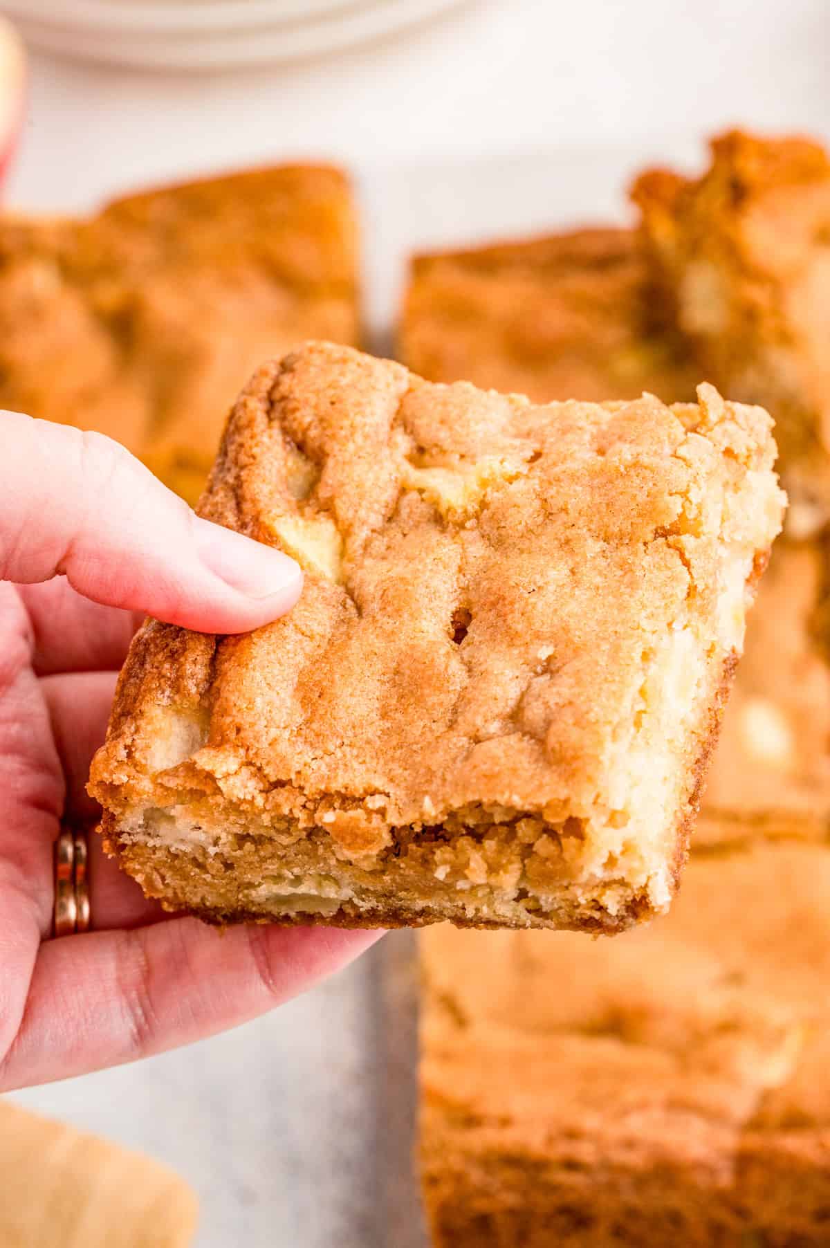 Hand holding up one of the blondies showing the apples inside.