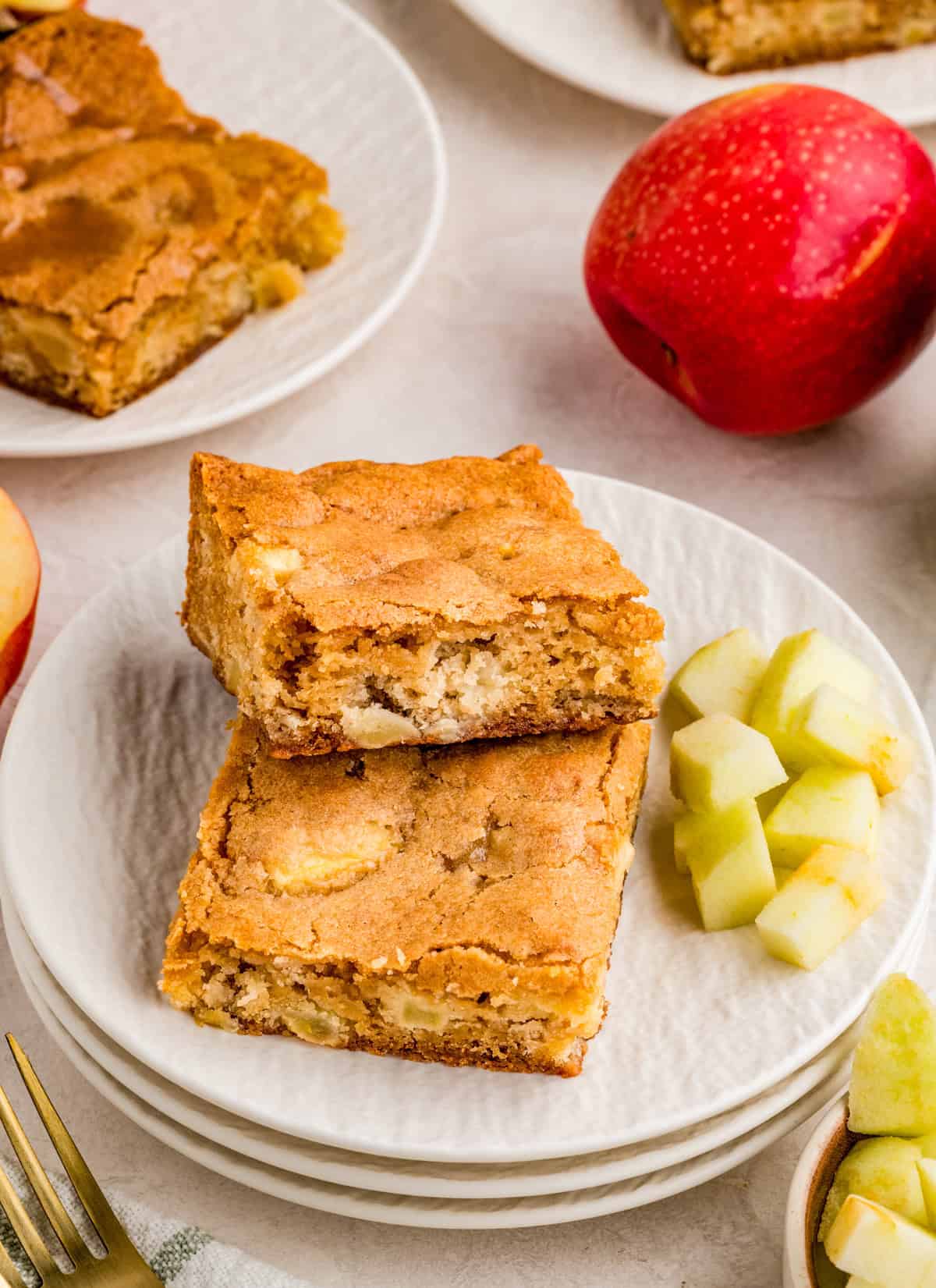 Two blondies on white plate layered on top of one another with diced apples on plate.