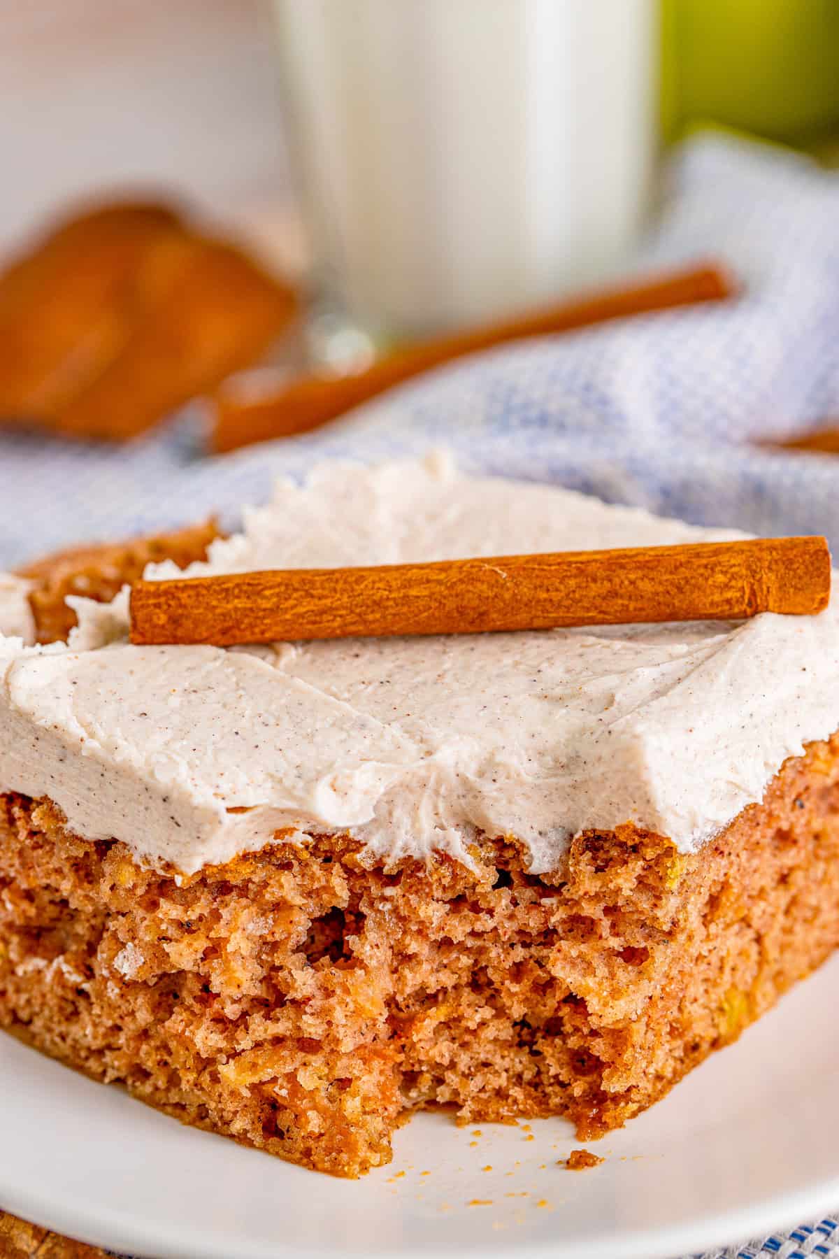 Cake on plate with a bite missing. Topped with frosting and cinnamon stick.