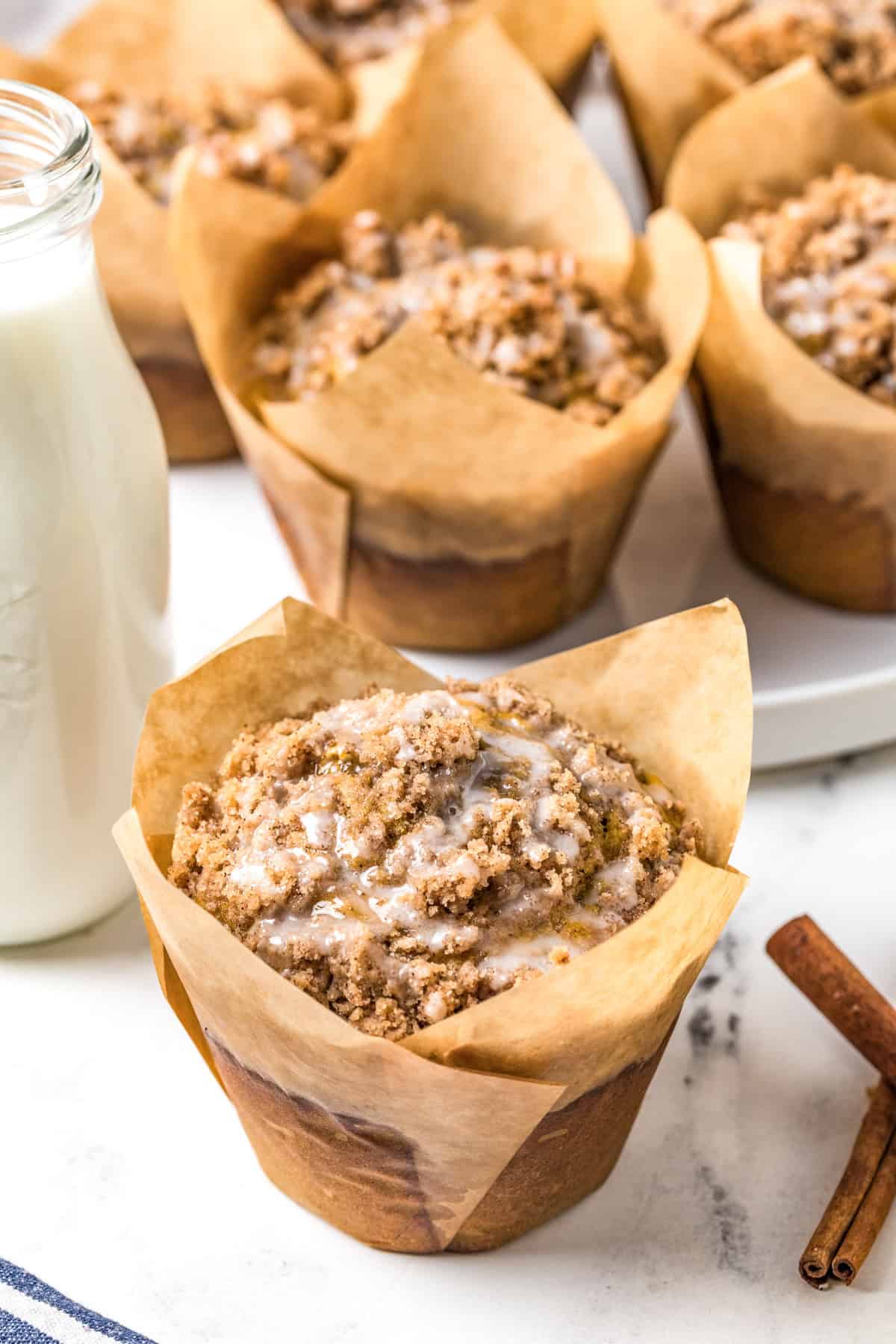 One of the finished Bakery Style Jumbo Pumpkin Banana Muffins in wrapper with more muffins in background with milk.