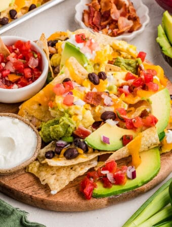 Close up square image of nachos on wooden round board with pico and sour cream.