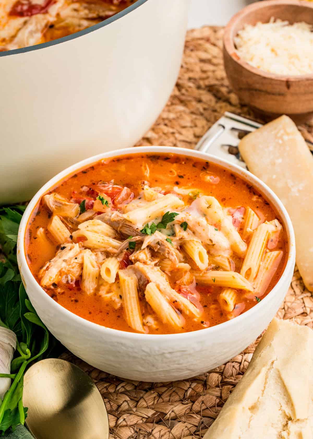 White bowl with Chicken Parmesan Soup topped with garnishes.