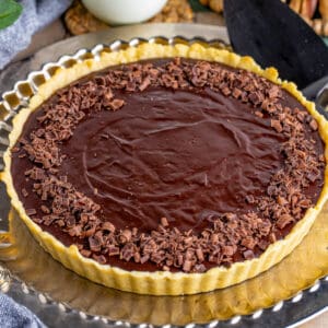 Close up square image of finished tart on gold serving platter topped with chocolate curls.