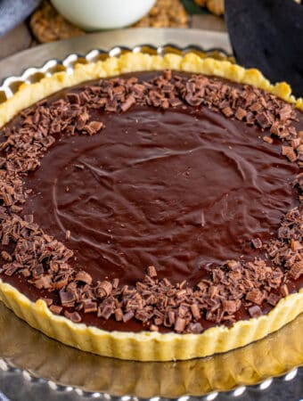 Close up square image of finished tart on gold serving platter topped with chocolate curls.