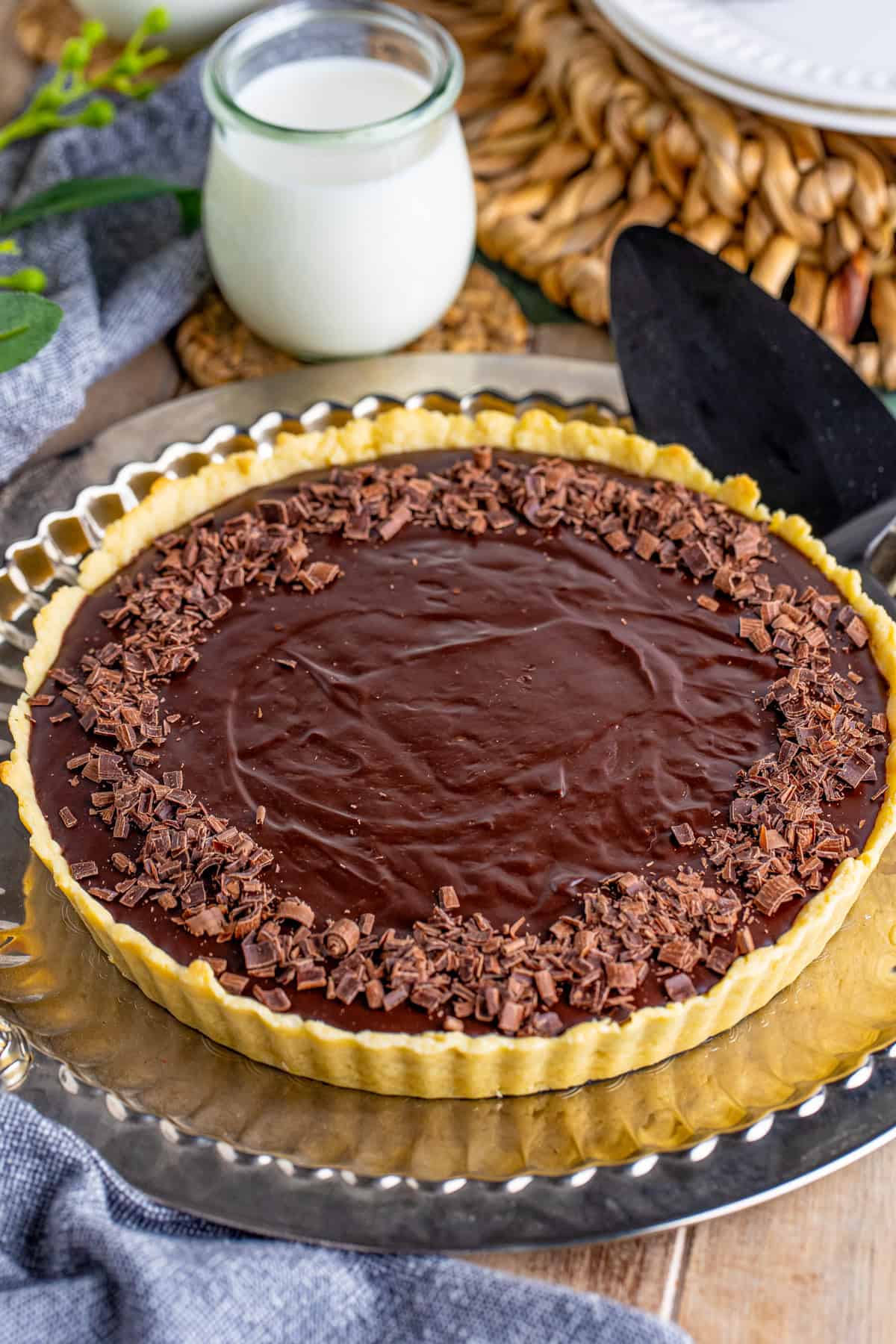 Finished Chocolate Ganache Tart on gold serving platter with chocolate curls and glass of milk in background.