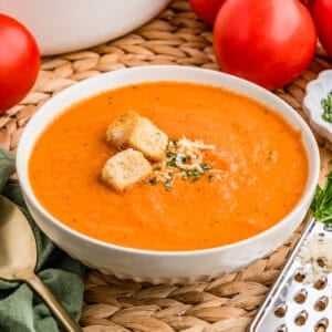 Close up square image of soup in white bowl topped with basil, cheese and croutons.