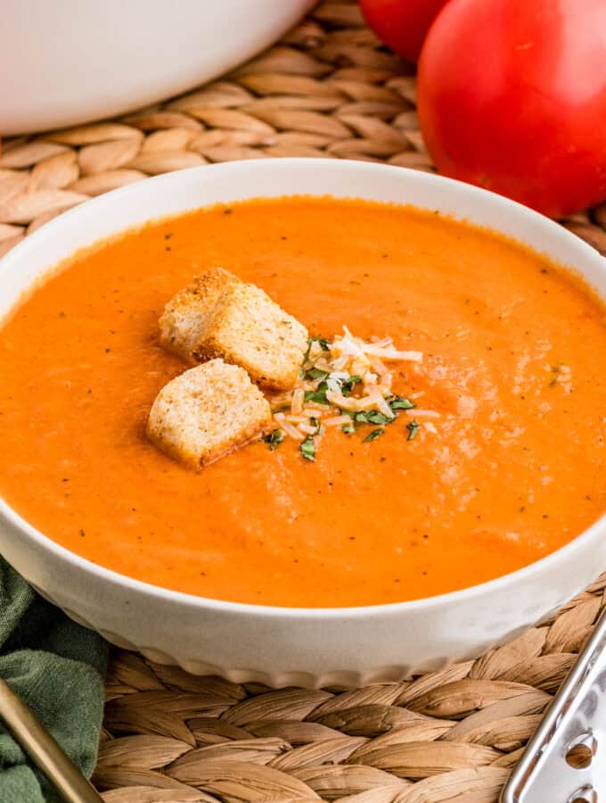 Close up square image of soup in white bowl topped with basil, cheese and croutons.