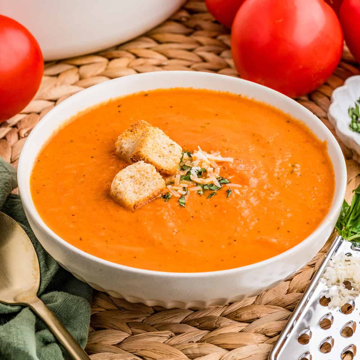 Close up square image of soup in white bowl topped with basil, cheese and croutons.