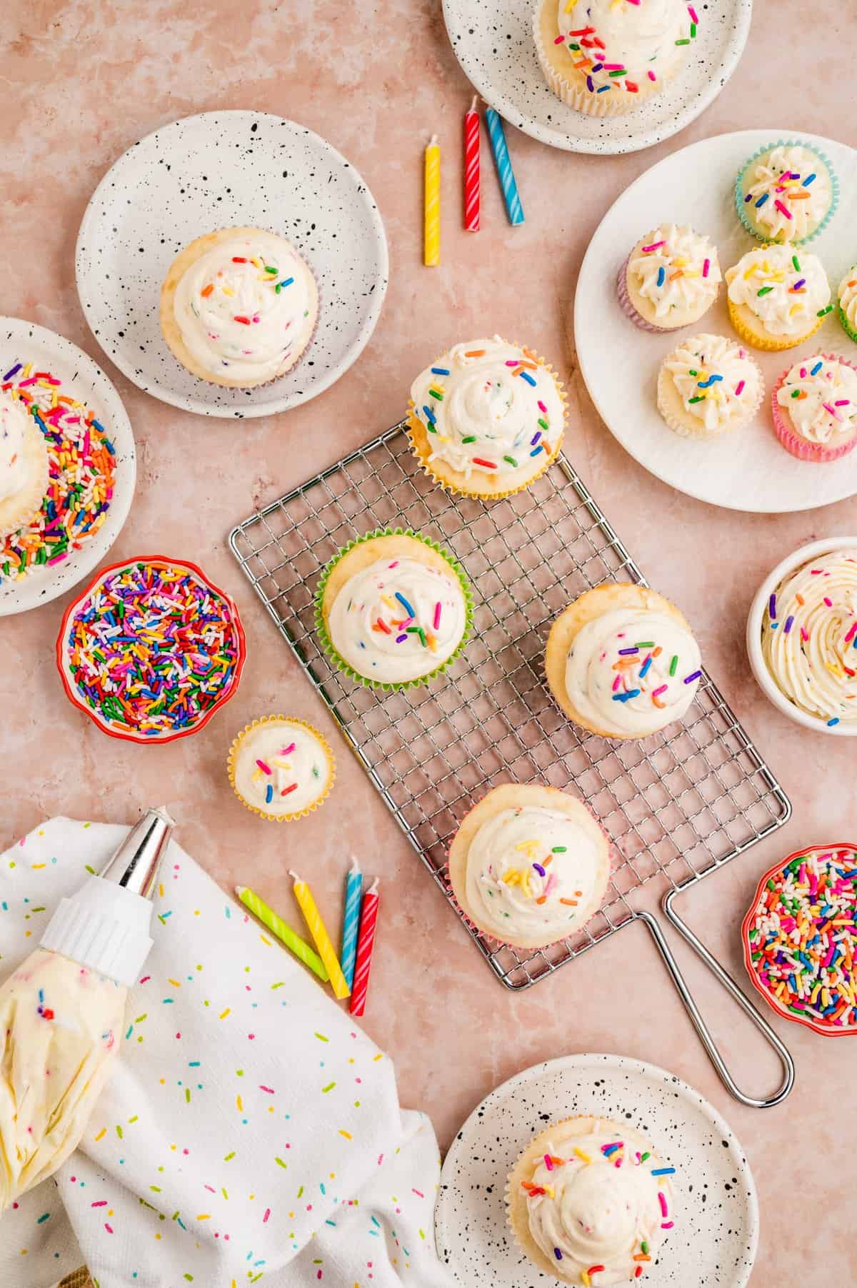 Overhead of finished frosting on cupcakes with bowls or sprinkles around cupcakes.