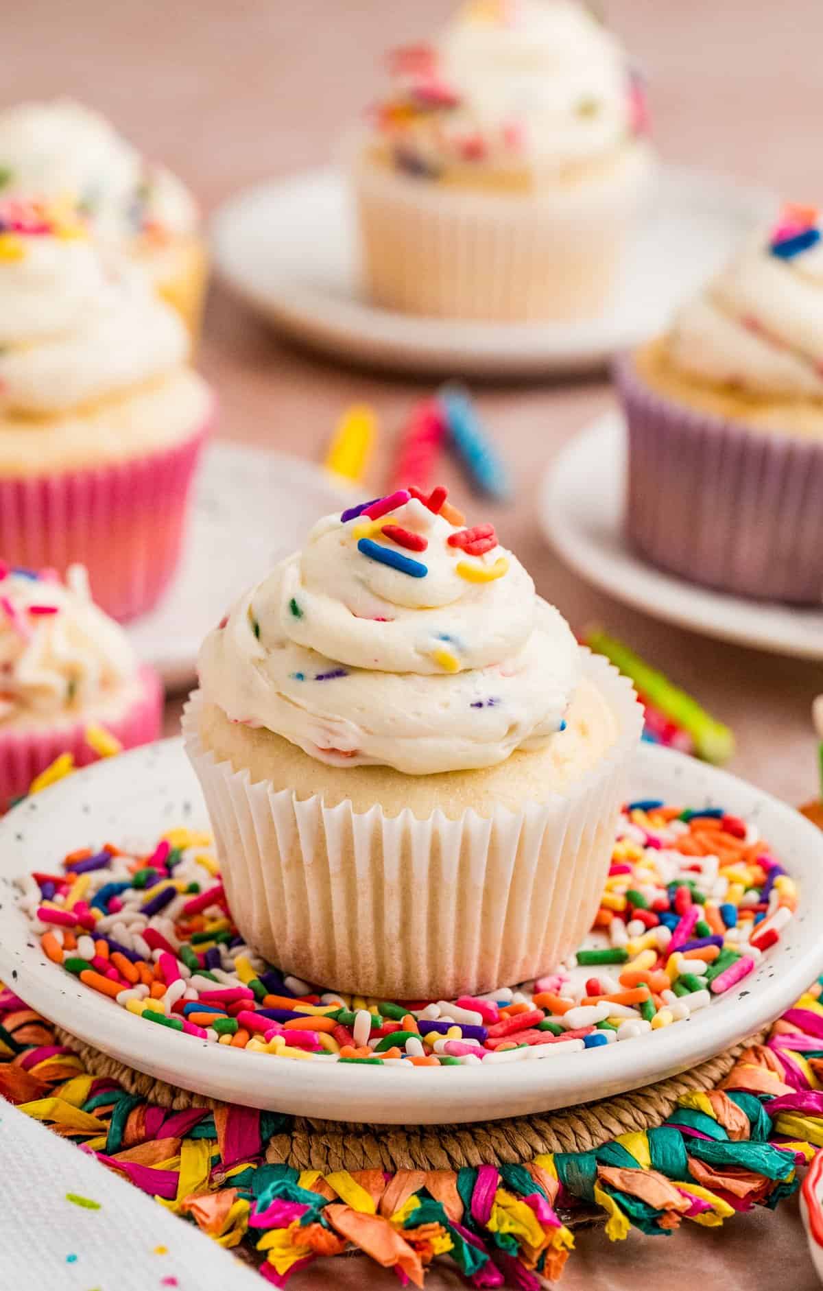 Funfetti Frosting on top of a cupcake on white plate filled with rainbow sprinkles.