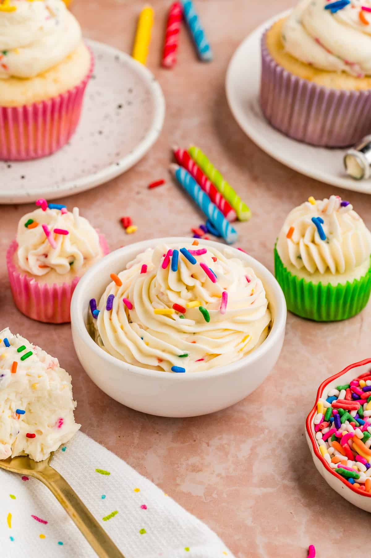 Frosting in a white bowl topped with sprinkles and spoon with more frosting on it.