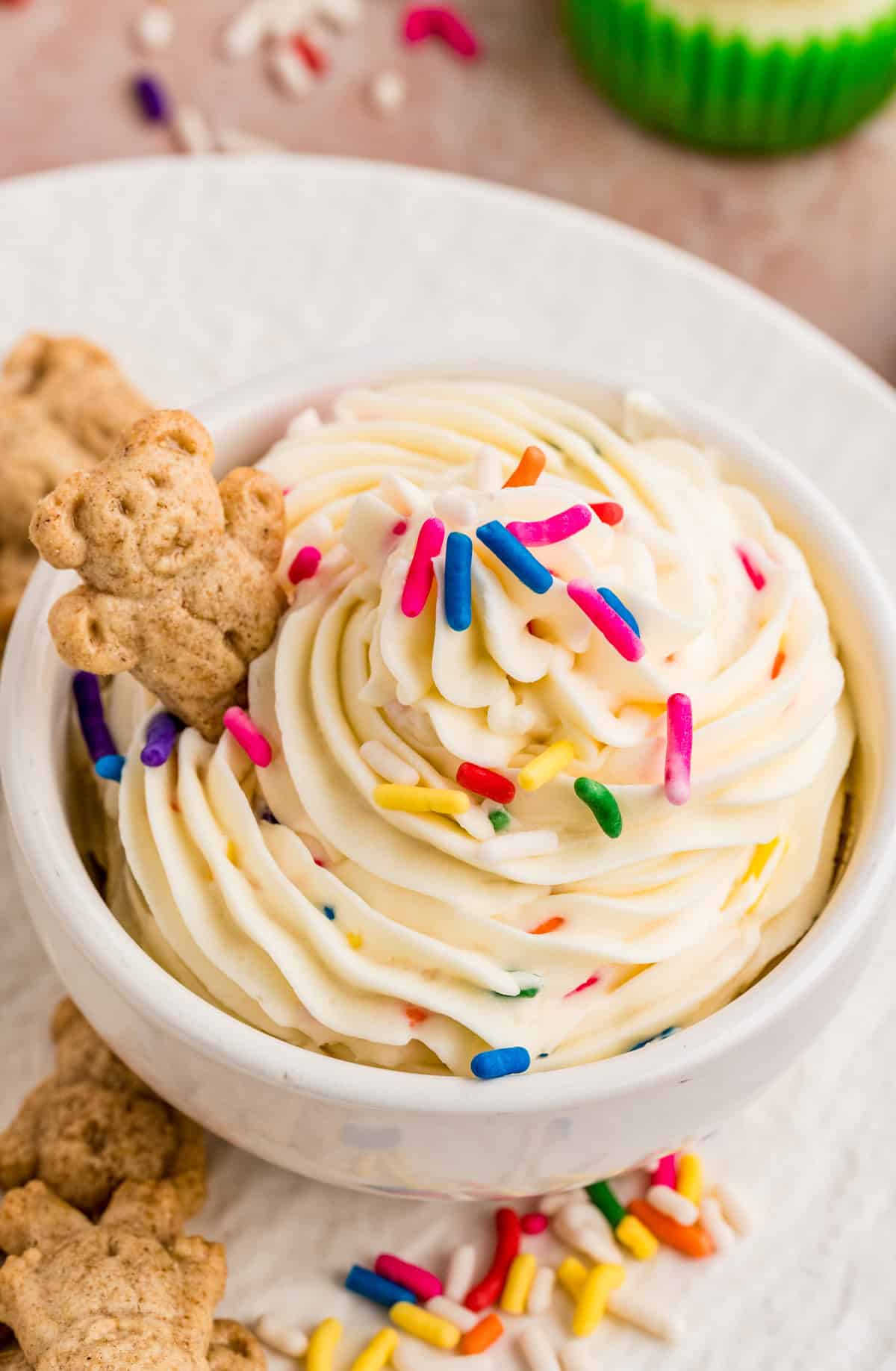 Close up of bowl of frosting topped with sprinkles and a graham cracker bear in bowl.