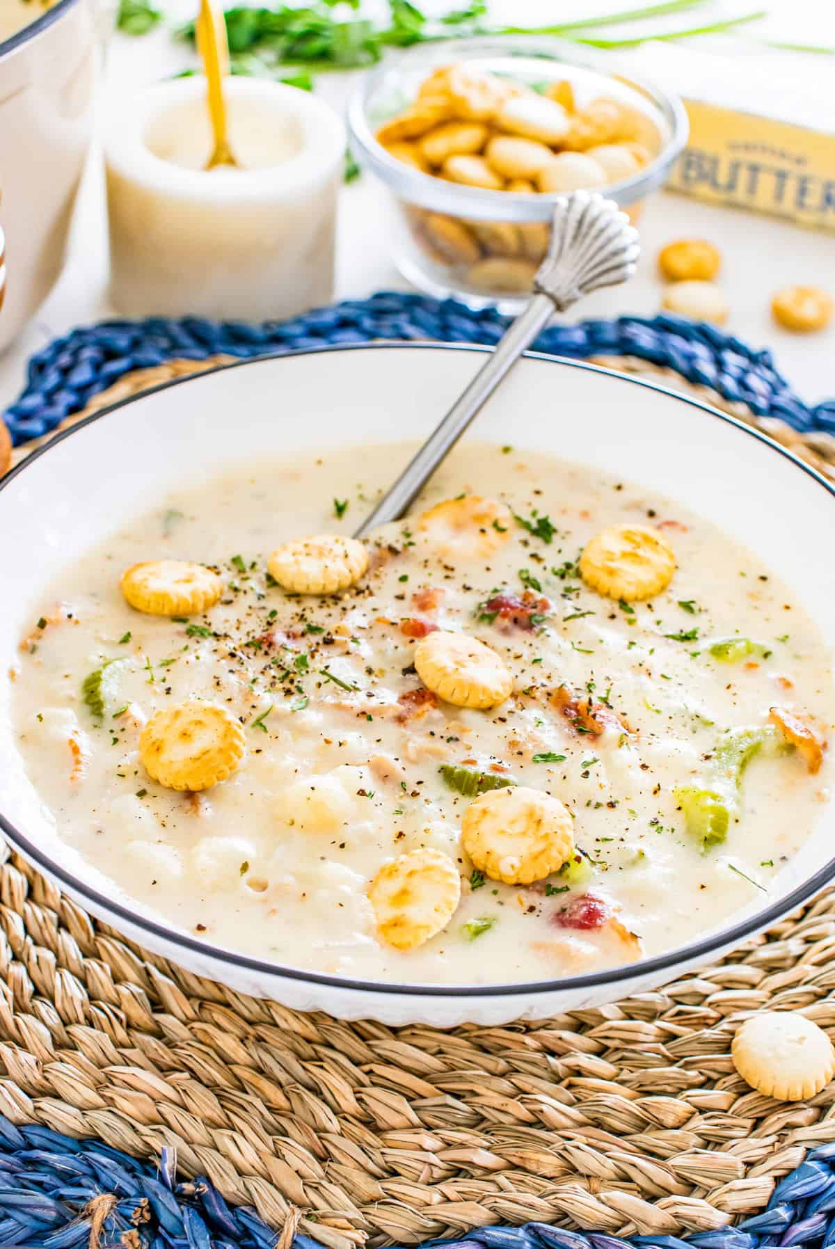 New England Clam Chowder in bowl with spoon, seasoning and oyster crackers.