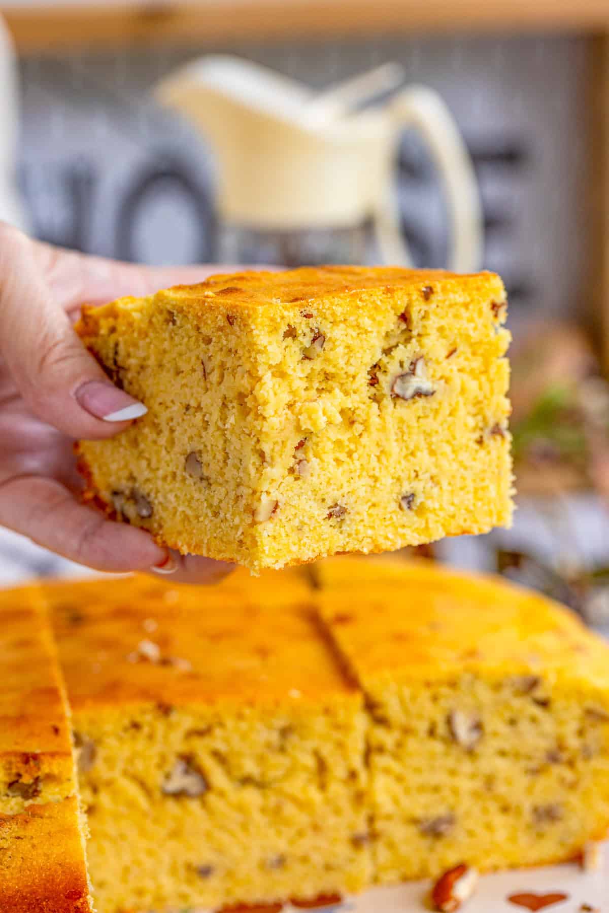 Hand holding up one piece of the Pecan Cornbread showing all the pecans inside.