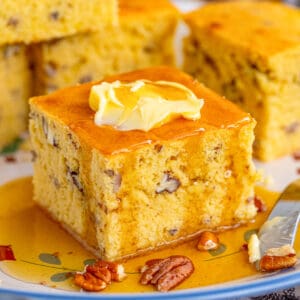 Close of of cornbread on plate with butter and syrup.
