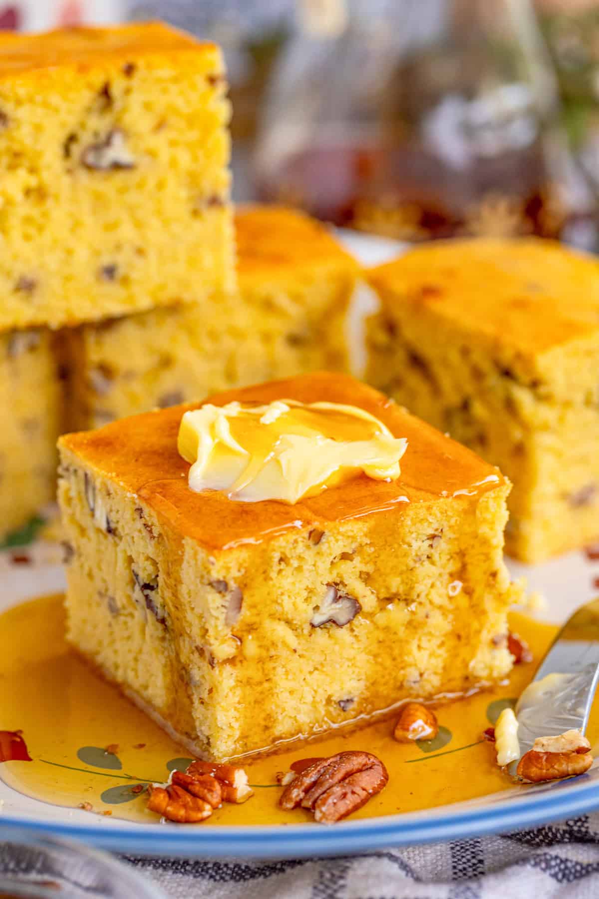 Finished Pecan Cornbread cut slice on plate topped with butter and syrup with more cornbread in background.