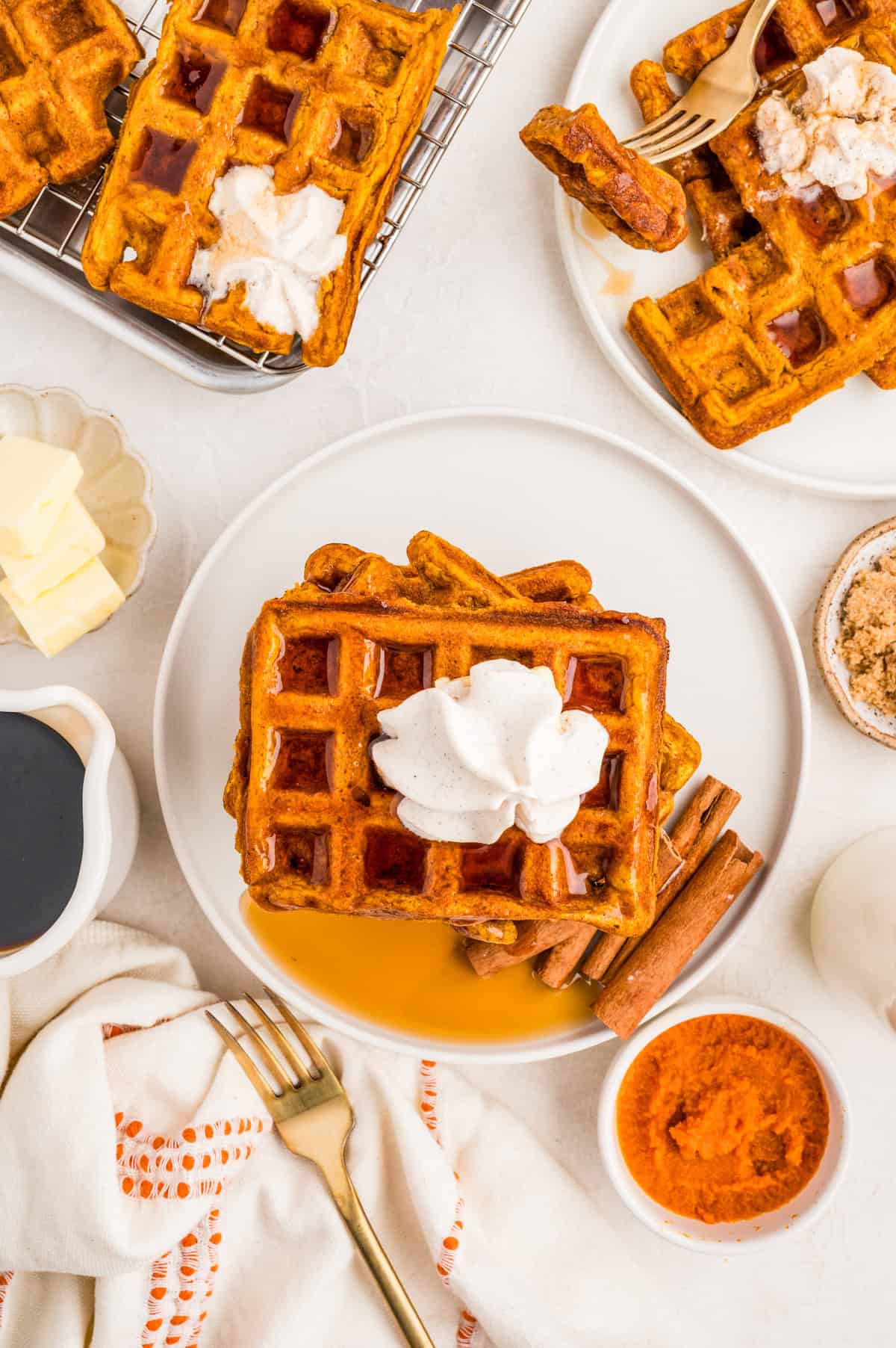 Overhead of Pumpkin Waffles topped with whipped cream and other ingredients around plates.
