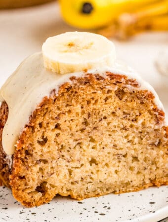 Close up of finished cake frosted and topped with a banana slice on a white plate.
