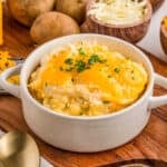 Square image of potatoes in a white handled bowl on wooden cutting board topped with parsley.
