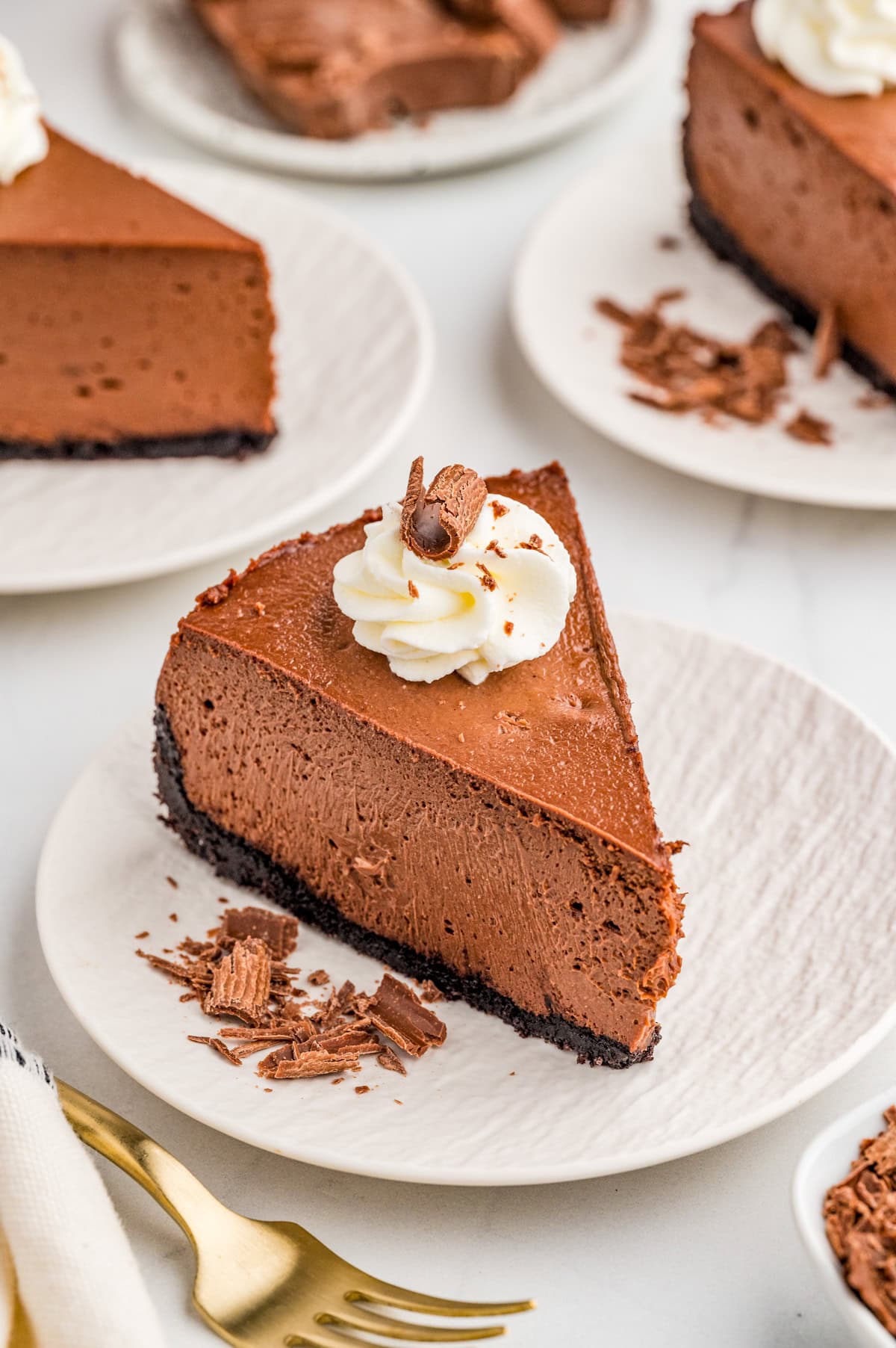 Slice of Chocolate Cheesecake decorated on white plate with chocolate shavings on plate.