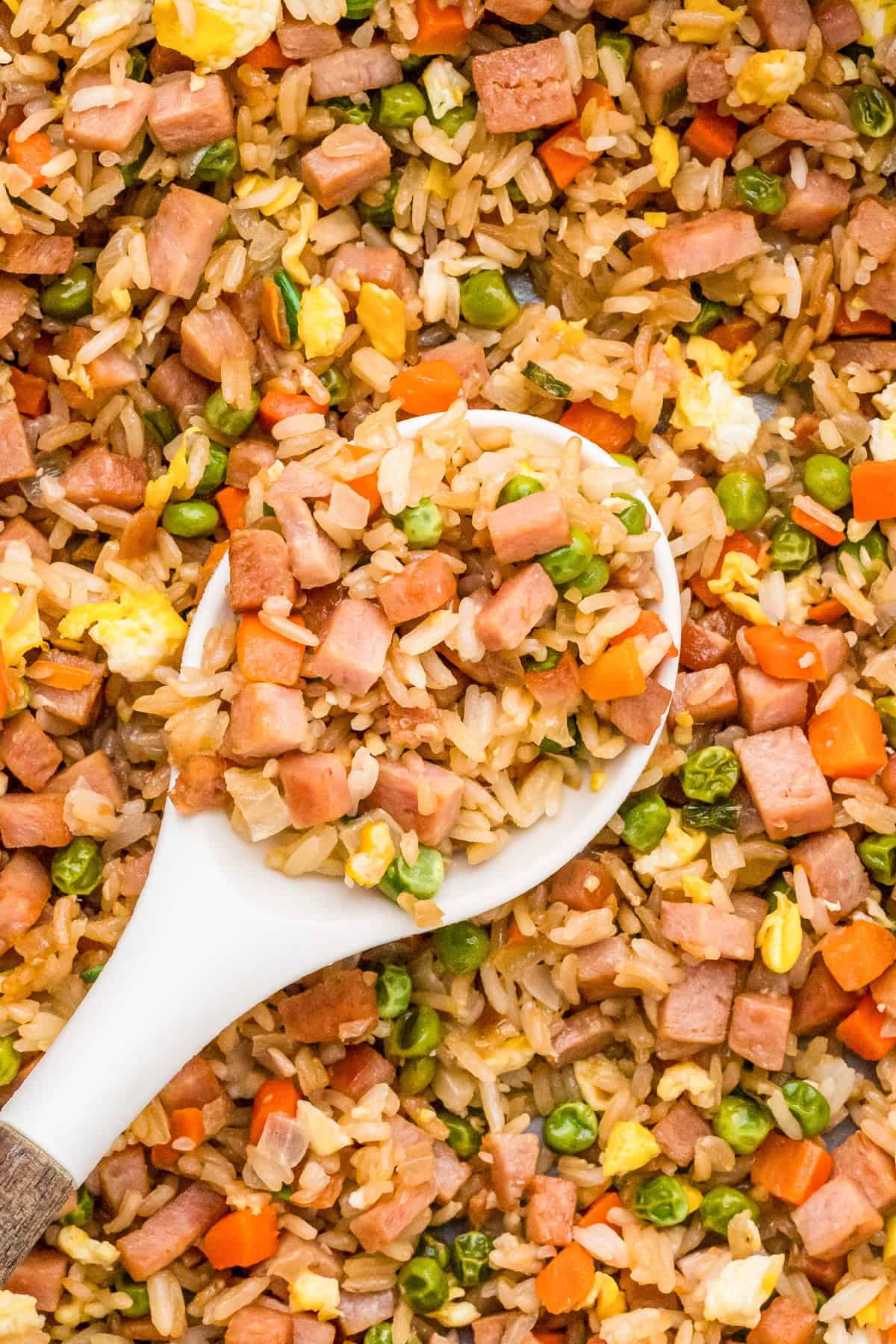 Overhead of spoon with some Easy Spam Fried Rice on it hovering over pan of the remaining fried rice.