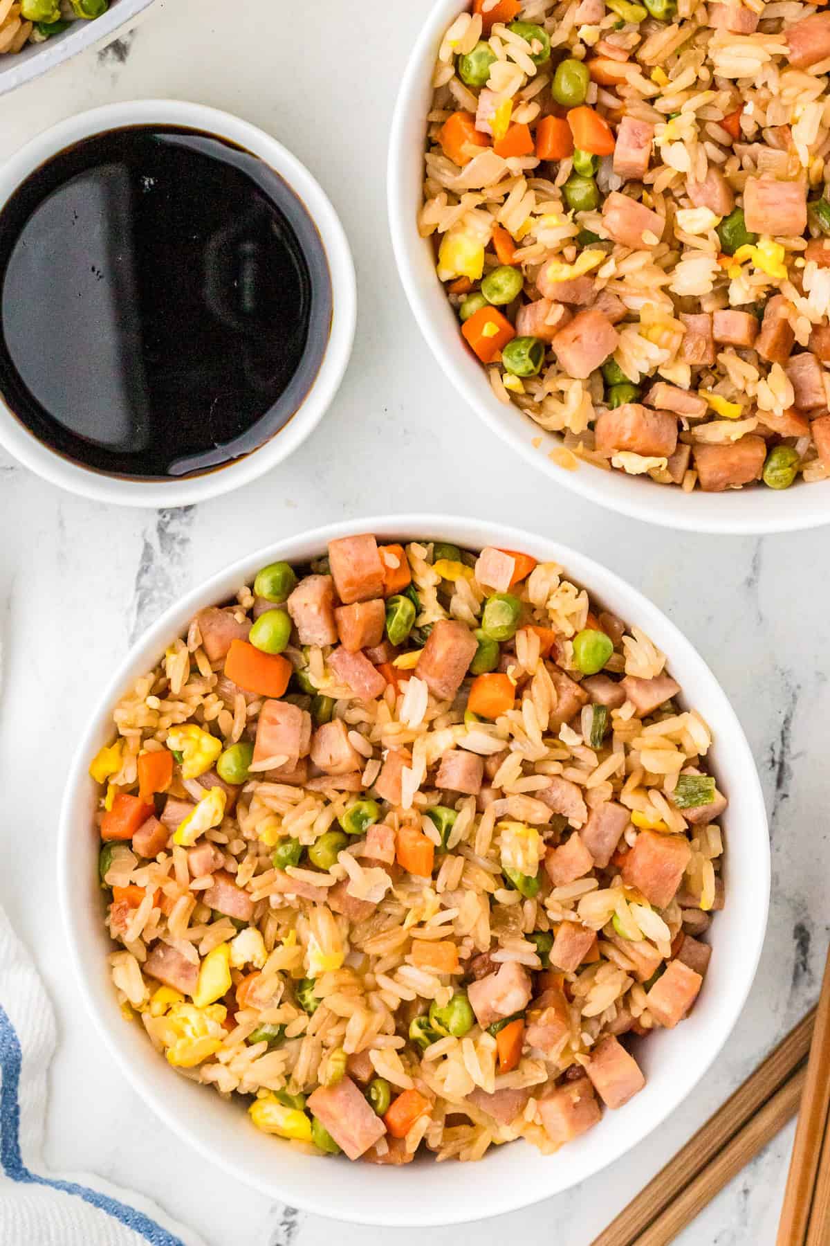 Overhead of two bowls of rice with soy sauce in another bowl.
