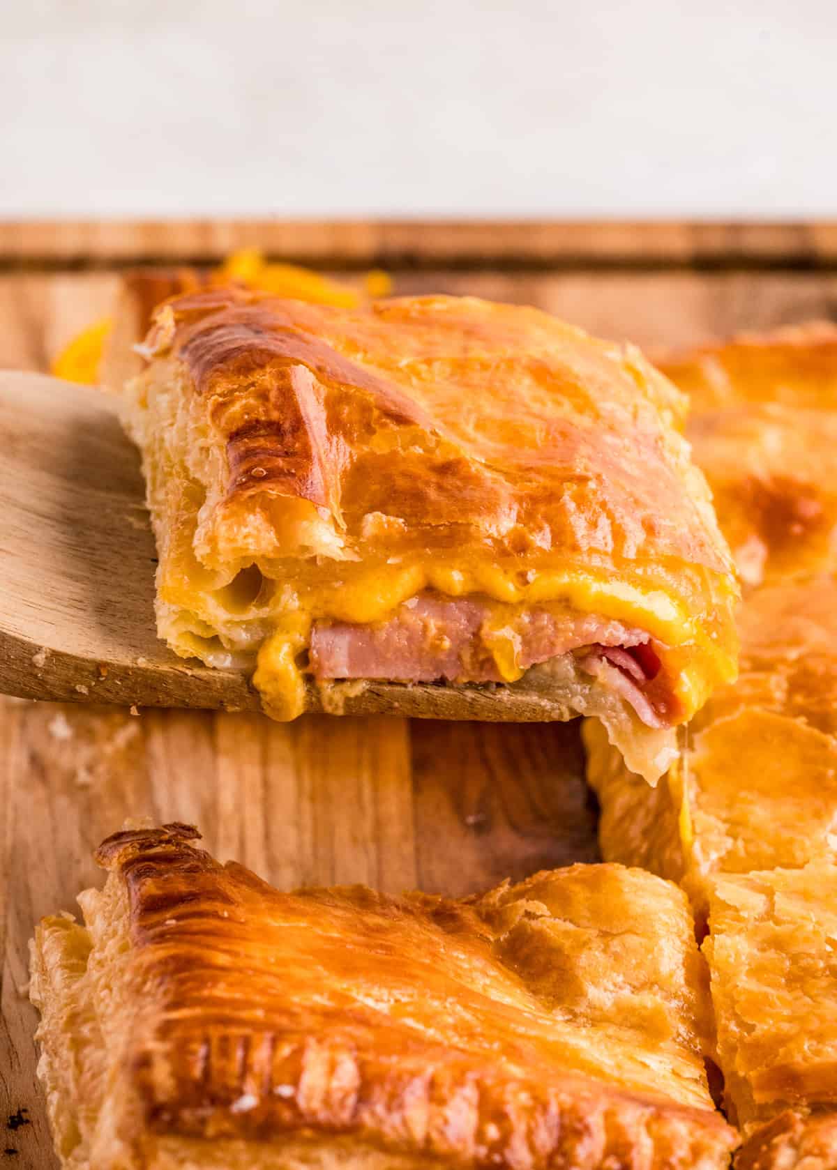 Wooden spatula lifting up one of the cut slices off of cutting board showing the melted cheese and ham.
