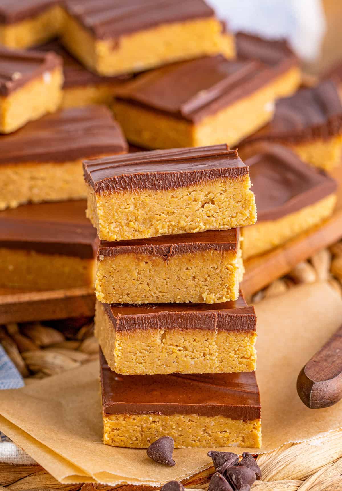 Four stacked No Bake Peanut Butter Bars on brown parchment paper in front of wooden board with more bars.