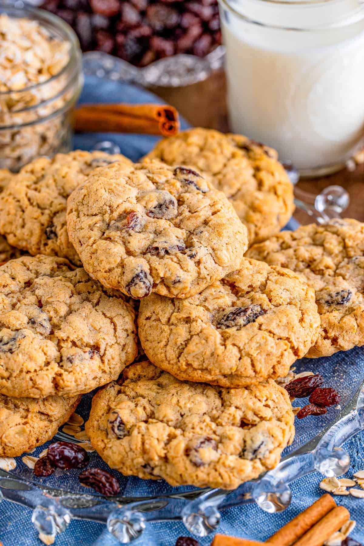Oatmeal Raisin Cookies stacked on blue linen with milk in background.