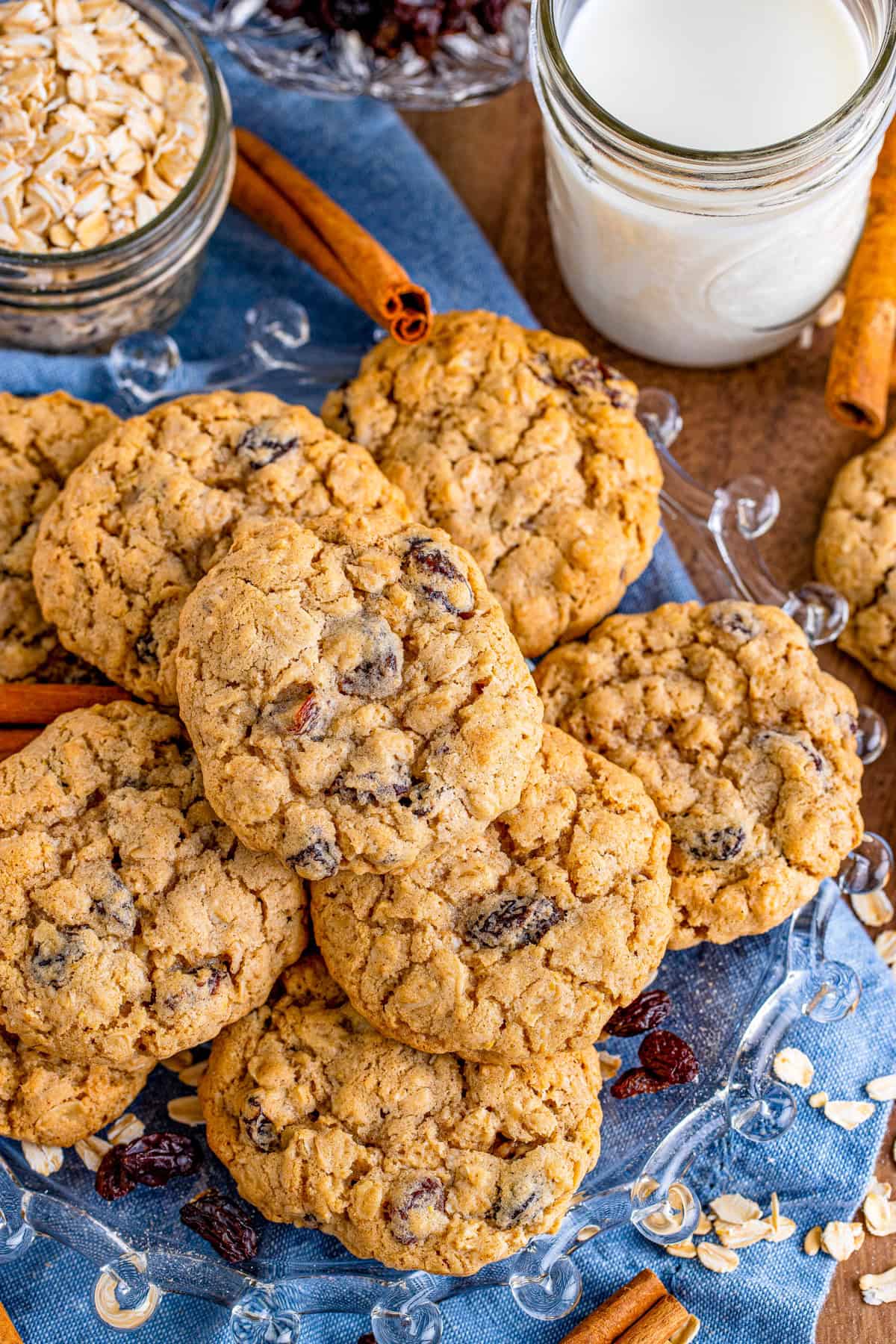 Overhead of stacked cookies on blue linen showing milk and oats.