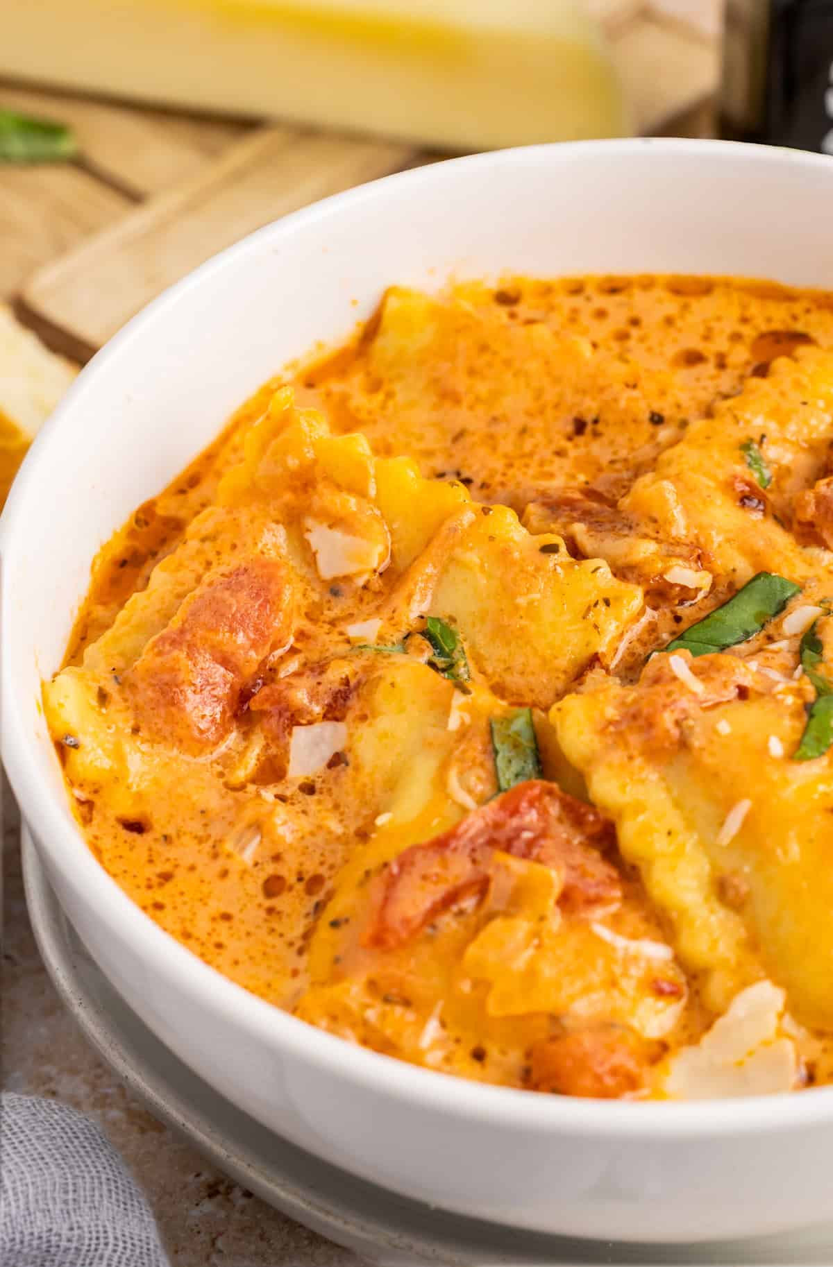Close up of soup in white bowl topped with basil and cheese.