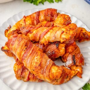 Close up square image of chicken tenders on white plate stacked on top of on another.