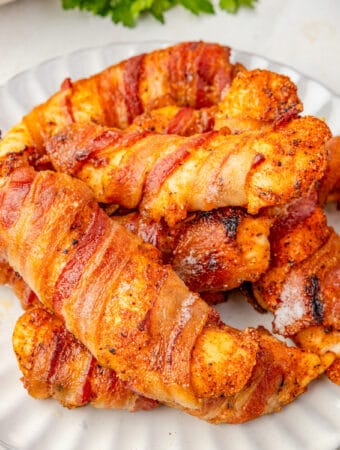 Close up square image of chicken tenders on white plate stacked on top of on another.
