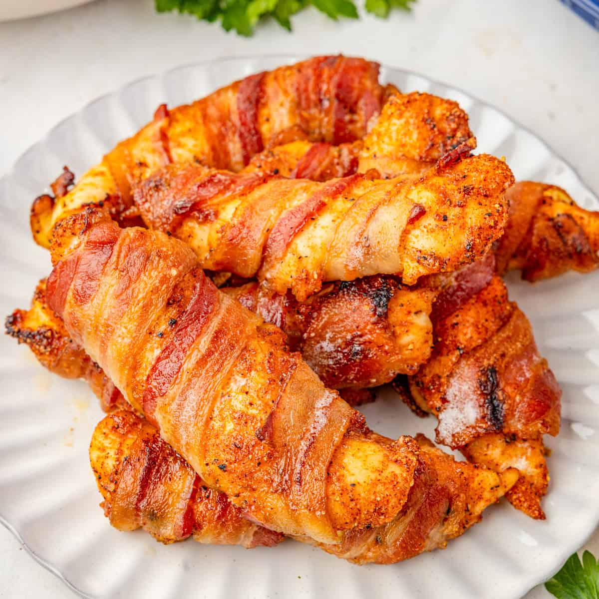 Close up square image of chicken tenders on white plate stacked on top of on another.