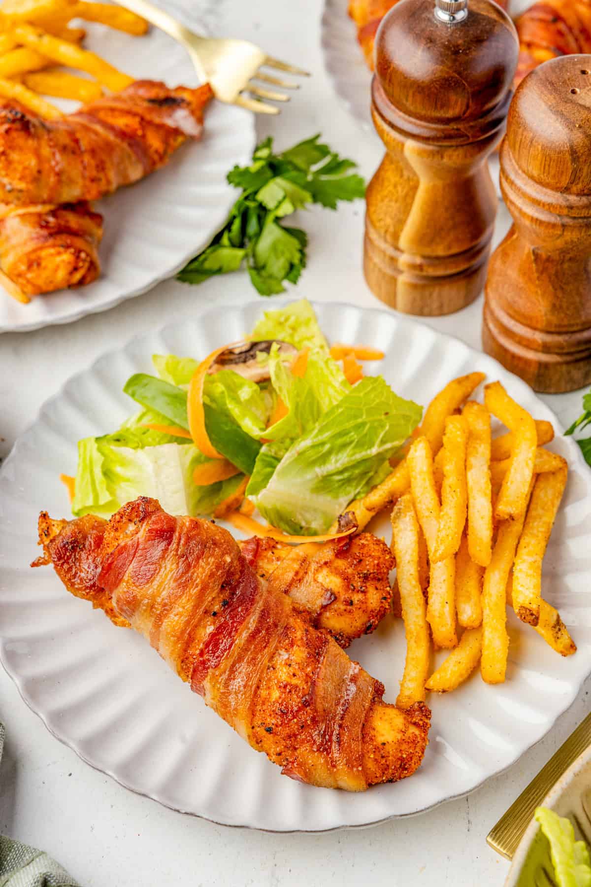 One chicken tender on plate with salad and french fries.