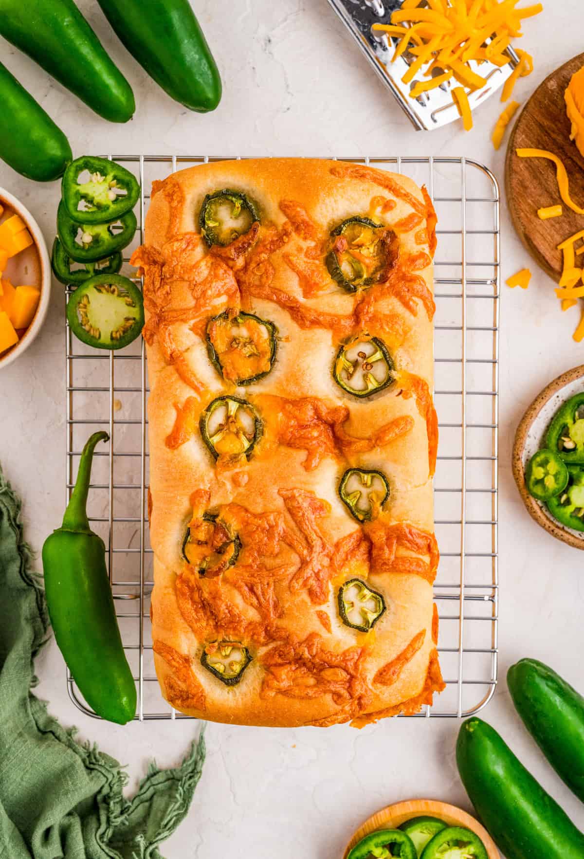 Overhead photo of finished bread on cooling rack with jalapeno and cheese next to rack.