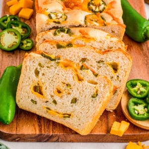 Square image of sliced bread on wooden board with jalapenos and cheese.