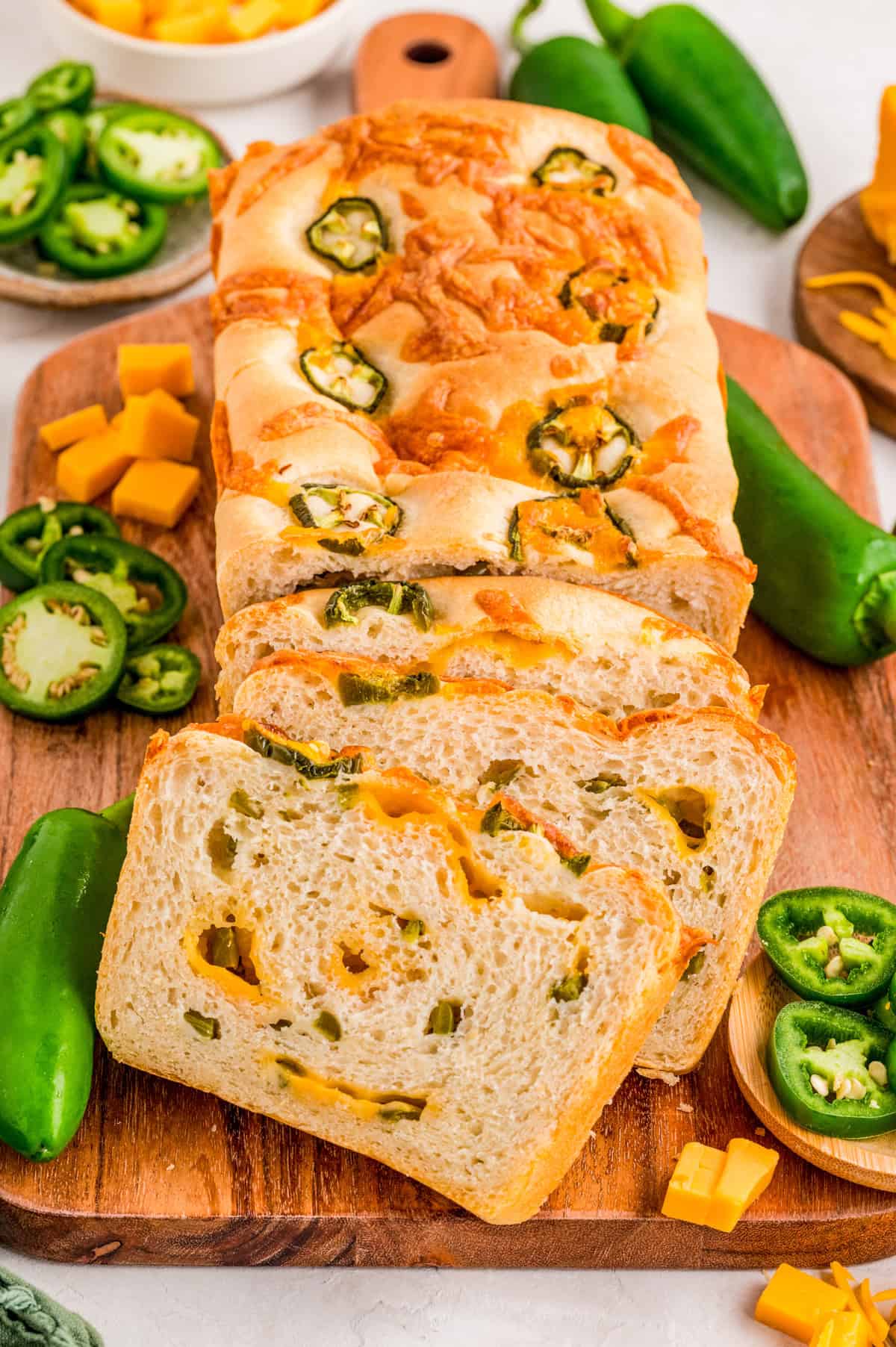 Sliced Jalapeno Cheddar Bread from loaf on wooden board with jalapenos and cheddar chunks.