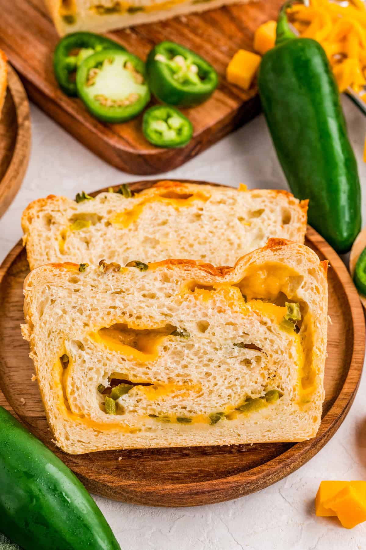 Two slices of bread on a wooden plate with jalapenos and cheddar cubes next to plate.